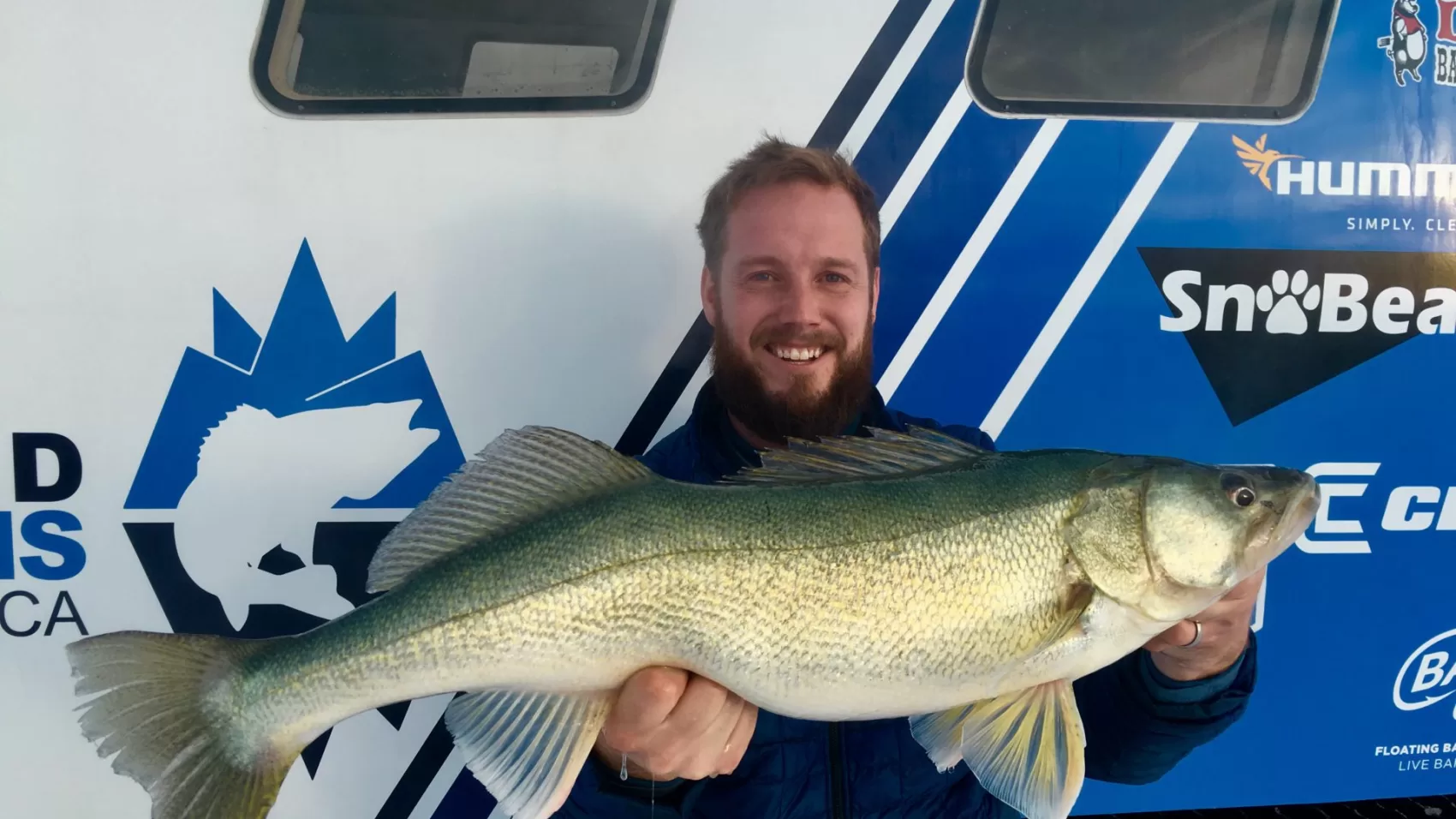 A man holding a fish in front of a boat.