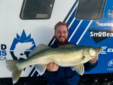 A man holding a fish in front of a boat.