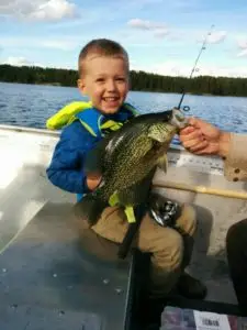 A boy holding a fish while sitting in the back of a boat.