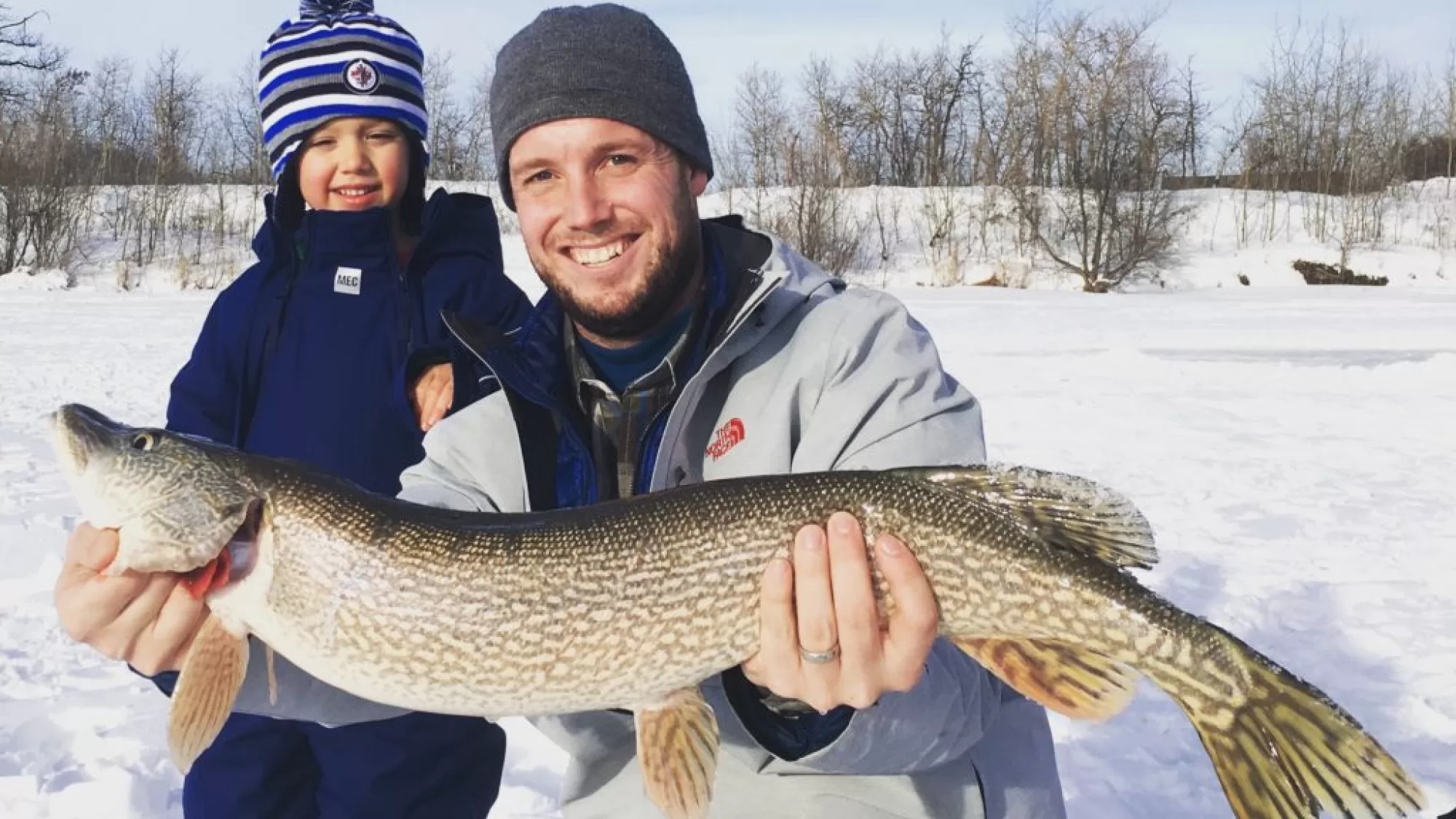 A man holding a fish while standing next to a child.