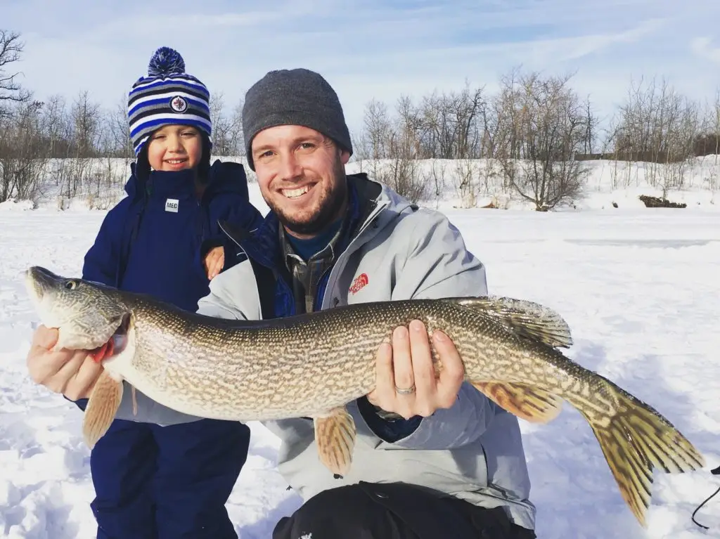 A man holding a fish while standing next to a child.